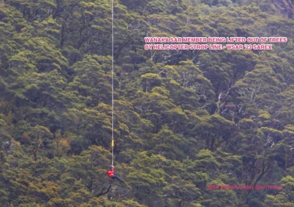 Wanaka SAR member being lifted from trees by helicopter strop line.